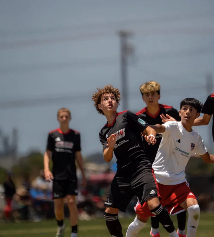 Soccer players battle for position as they track a ball overhead.