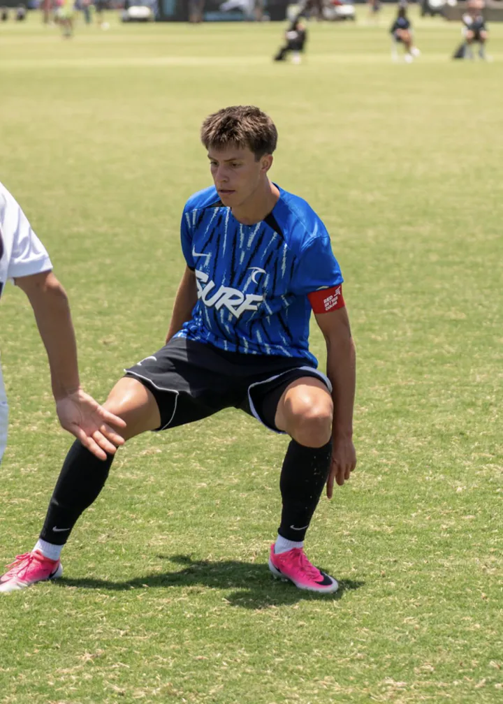 Soccer player in a blue jersey drops into a defensive stance on the field.