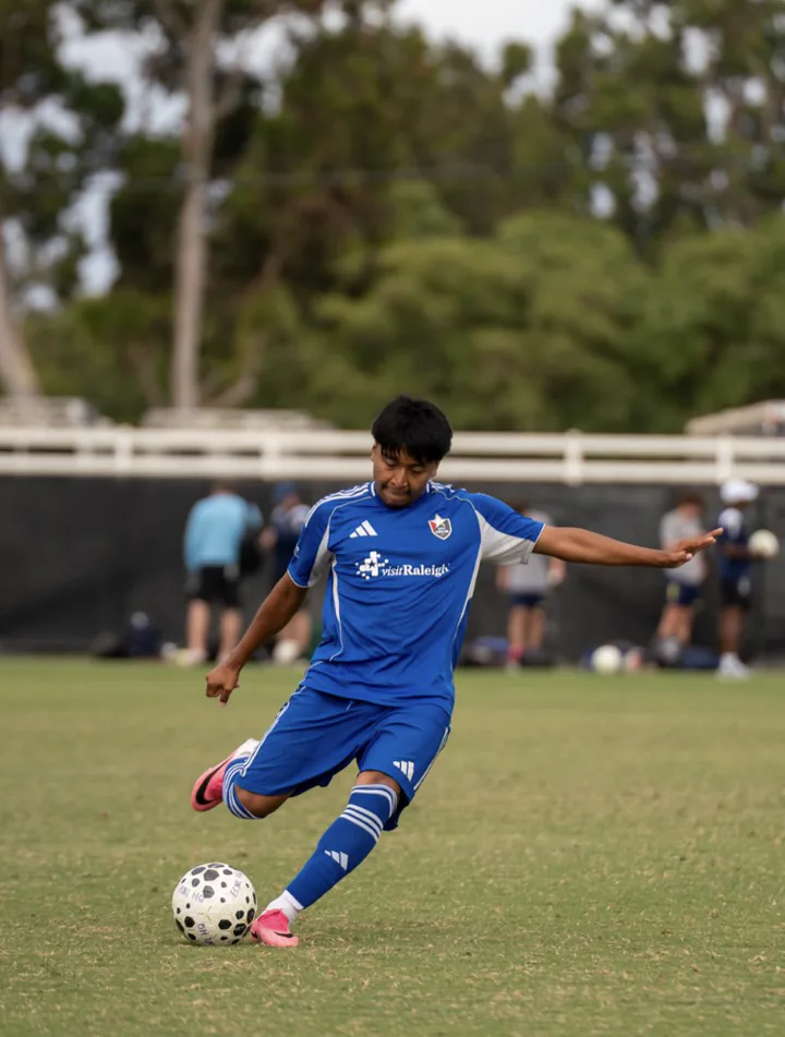 Soccer player in a blue kit striking the ball during a match.